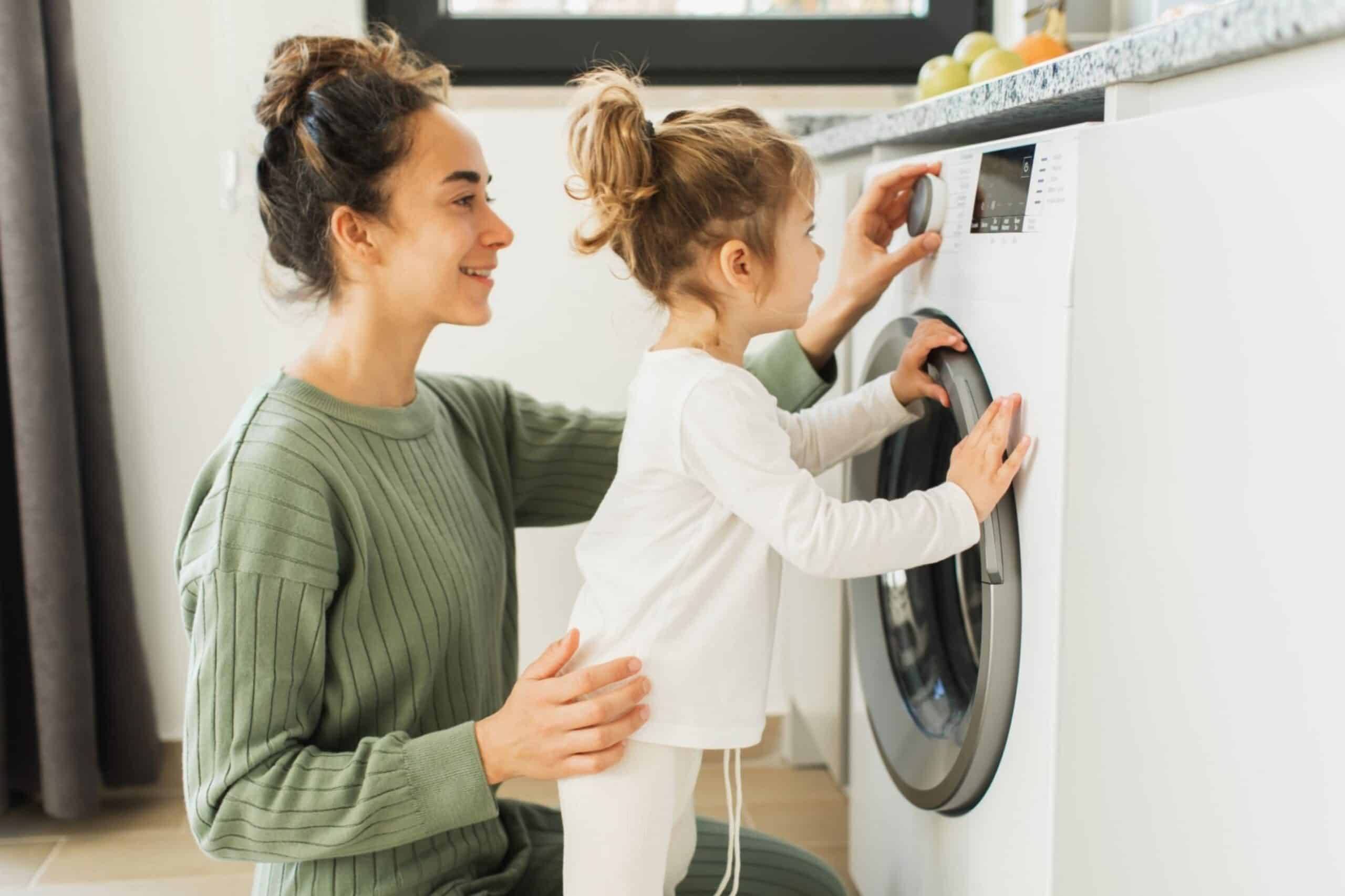 Mother and child girl little helper loading washing machine