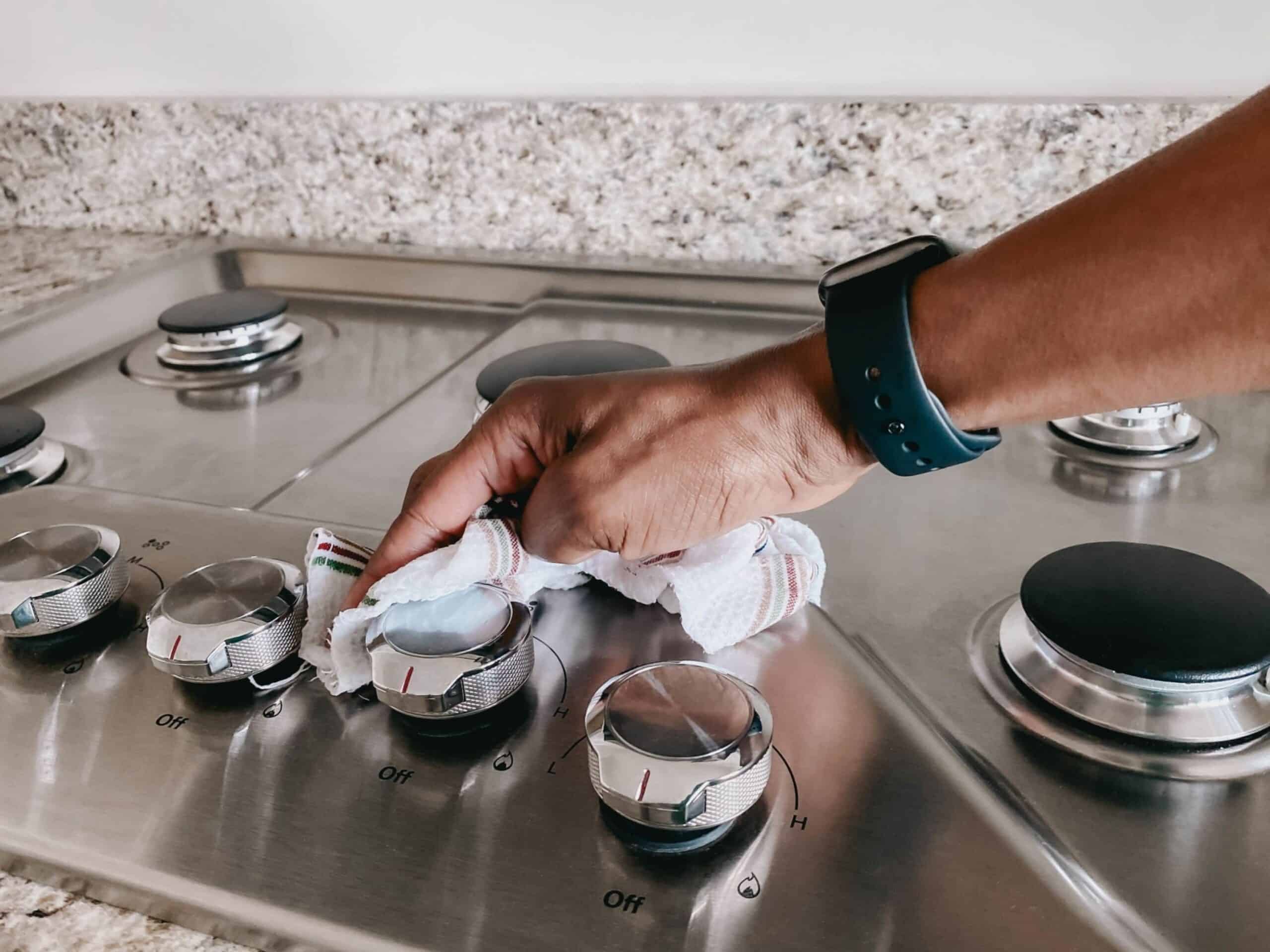 man's hand wiping down cooktop with wet dishcloth