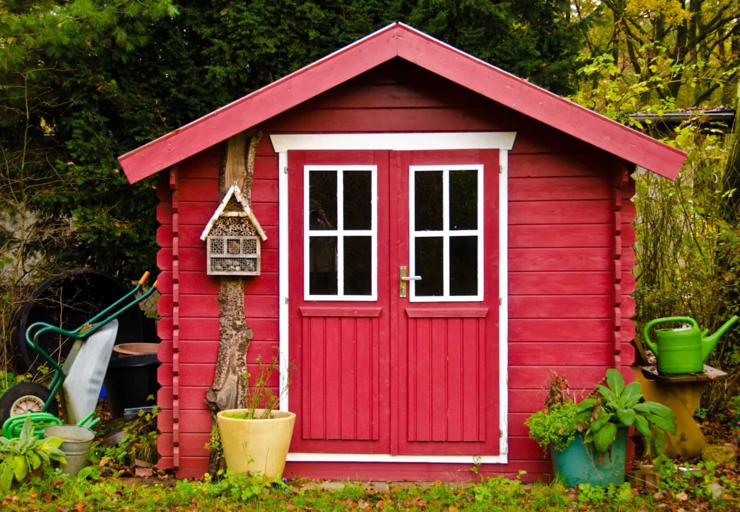 A light red small shed, gardenhouse, with some garden tools around it