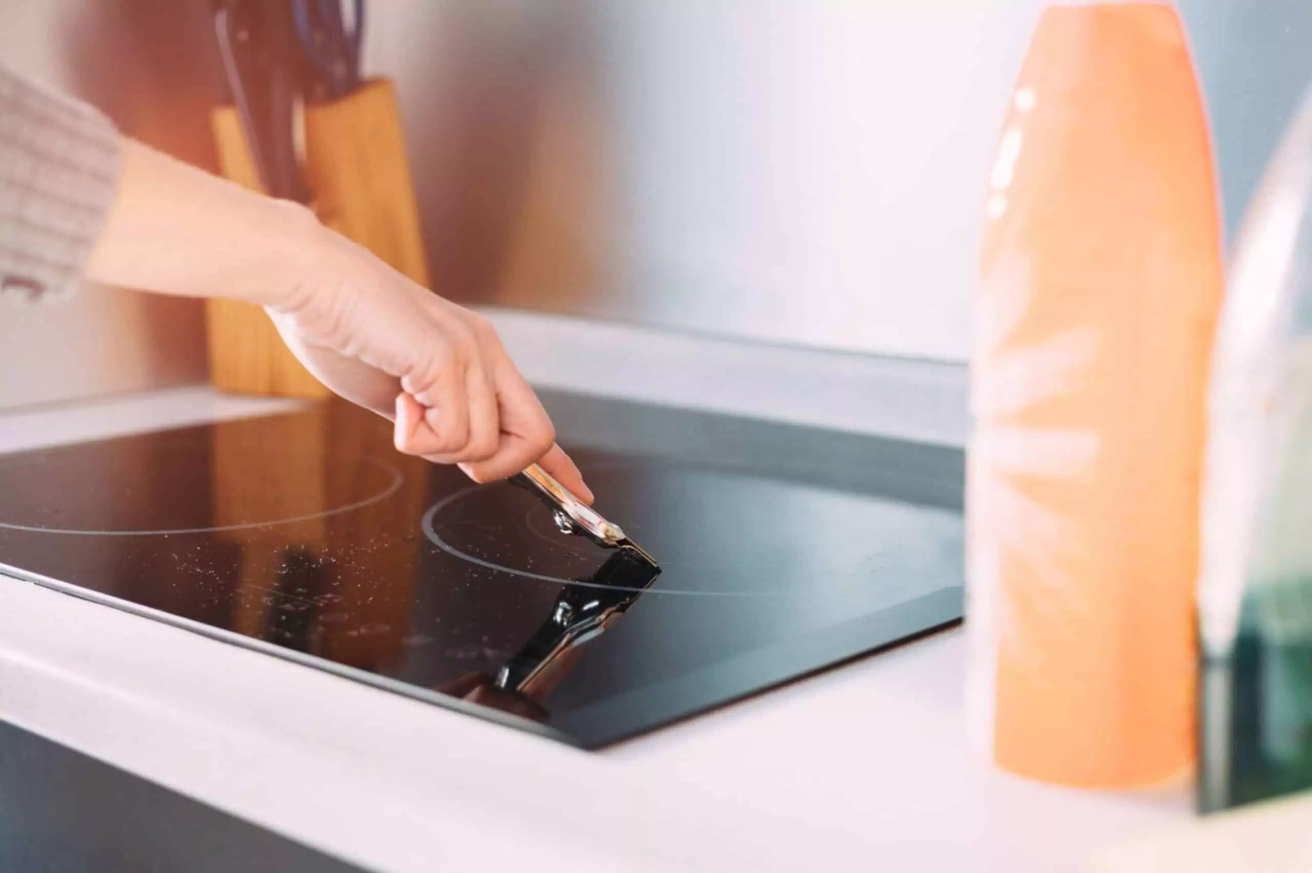 Female hand cleaning dirty induction stove with scraper